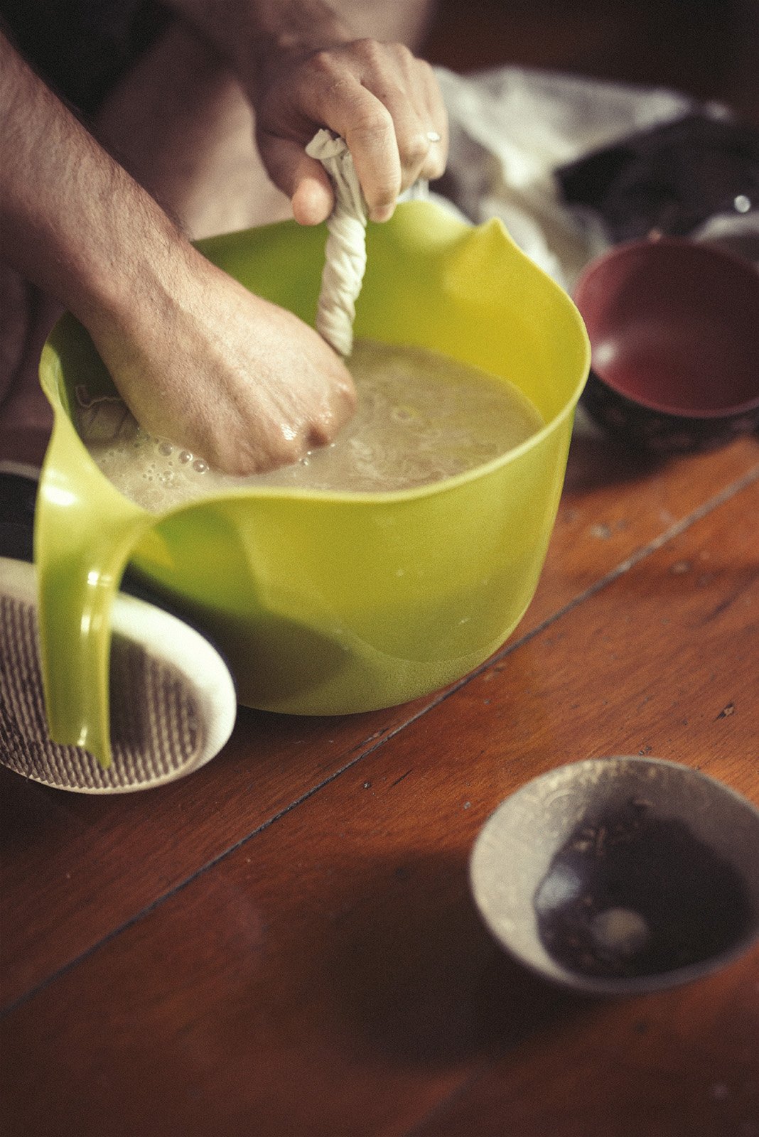 Hands kneading a strainer bag of kava in a wooden bowl, in Forney Enterprises' Vanuatu facility